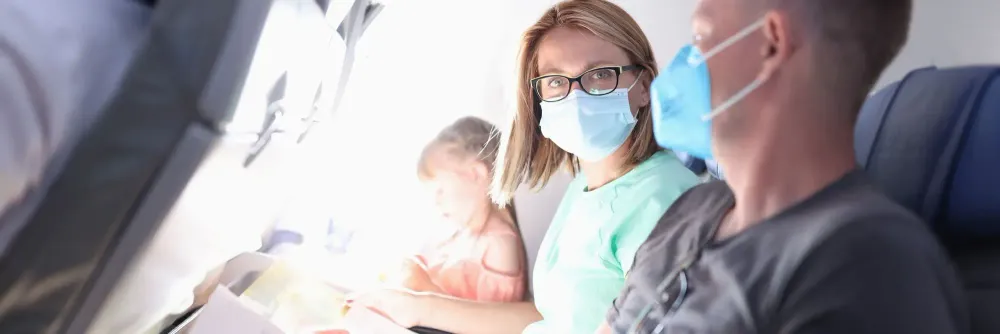 Two adults and a child sitting in a row on a plane, the adults are wearing medical face masks